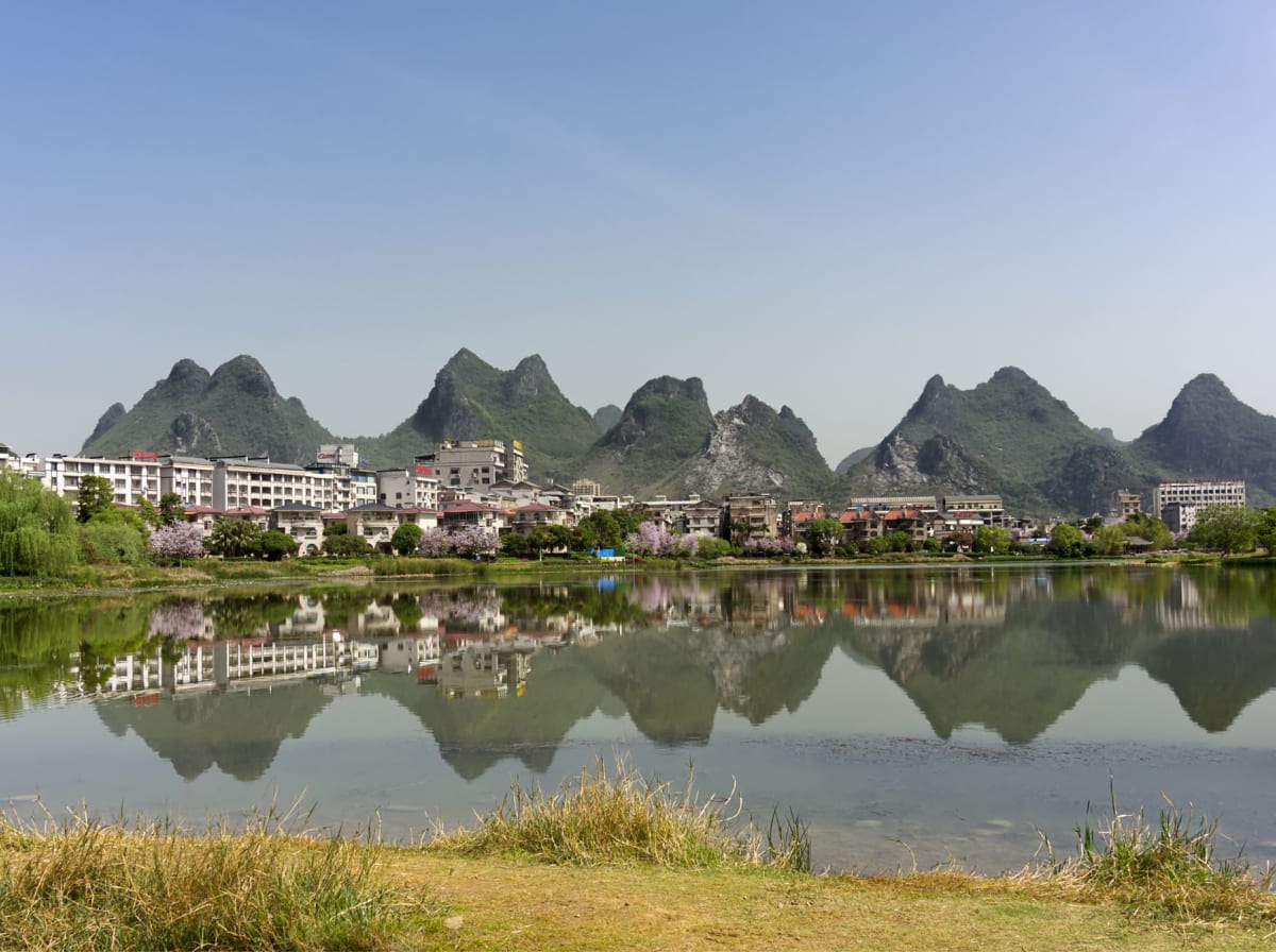 Cintas de niebla entretejiéndose entre sucesivas hileras de picos kársticos sobre el meandro plateado del río Li, iluminadas por el amanecer desde la colina Xianggong