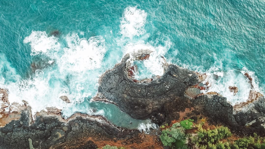 Queen's Bath tide pool carved into black lava rock with clear turquoise water pooling inside on a calm day
