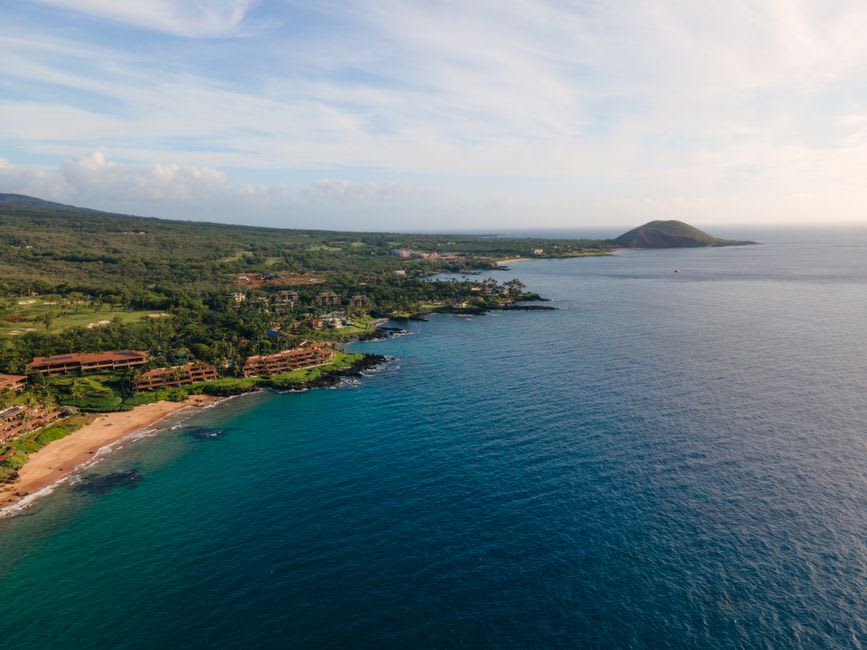 A rocky lava point between two beaches on the Wailea coast, tide pools visible in the foreground with the ocean and distant islands beyond