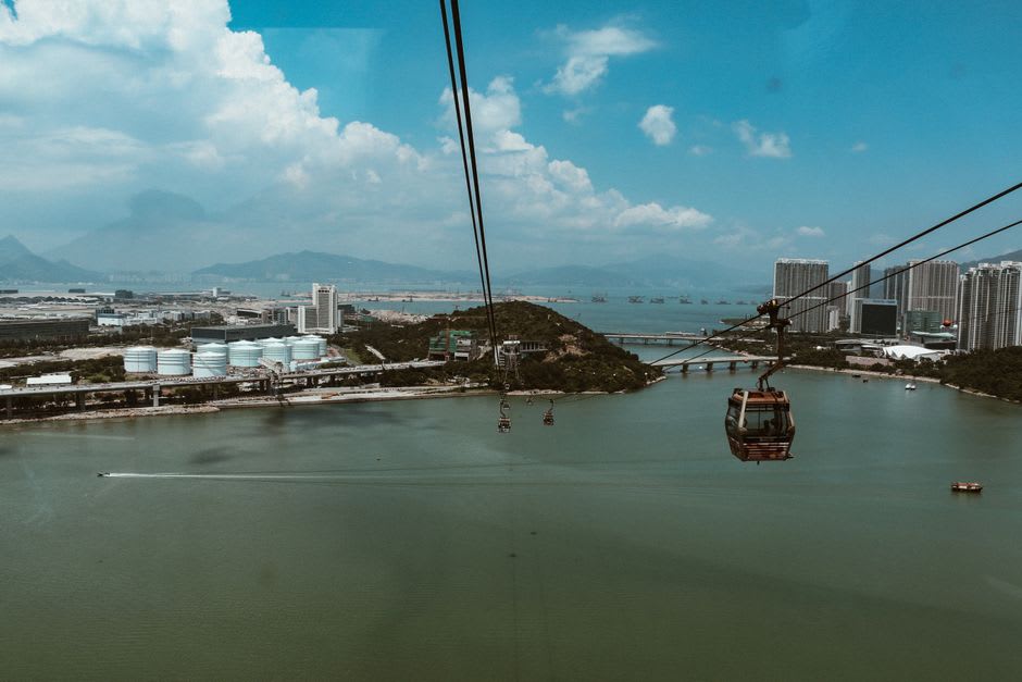 Le téléphérique de Ngong Ping traversant les collines boisées de l'île de Lantau, des porte-conteneurs visibles au loin en contrebas