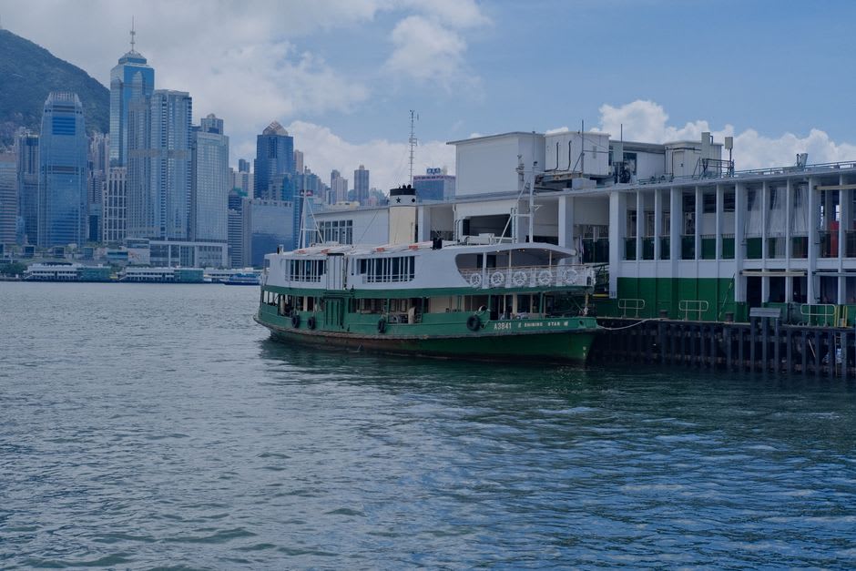 Le pont en bois et les rambardes vertes d'un bateau du Star Ferry traversant le port, Kowloon s'estompant derrière