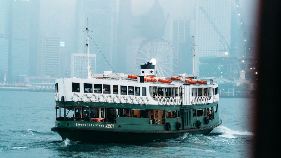 Des passagers sur le pont supérieur du Star Ferry regardant la ligne d'horizon de l'île de Hong Kong défiler au coucher du soleil
