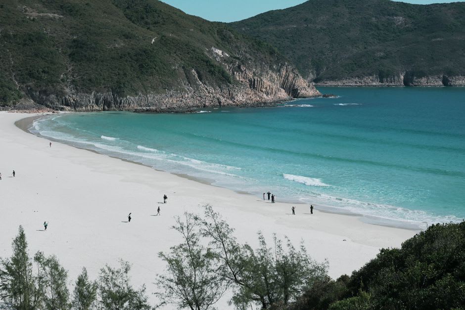 El sendero hacia Tai Long Wan cruzando ladera abierta, la hilera de playas visible mucho más abajo