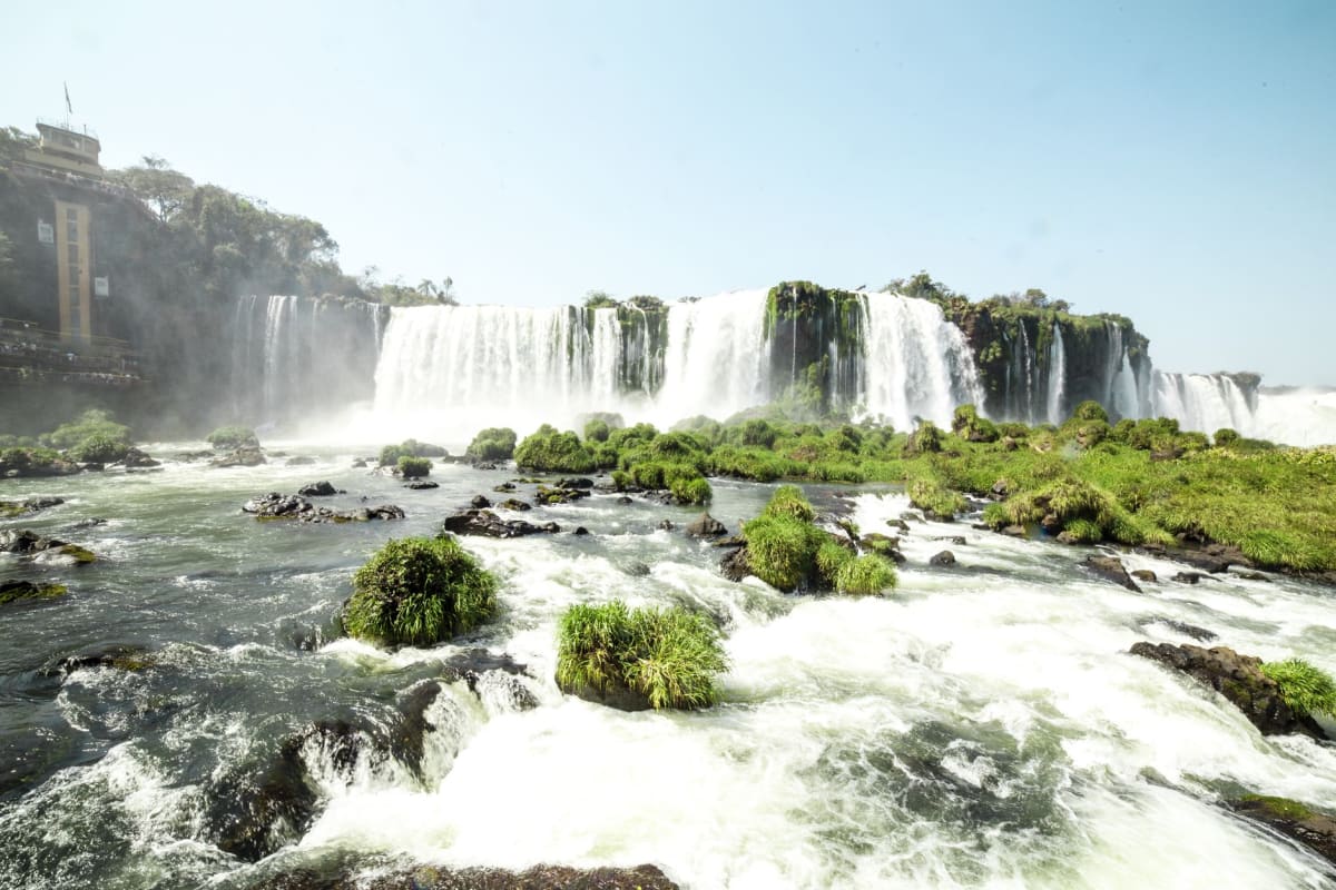 Los canales del vertedero abiertos de la represa Itaipú con agua blanca agitándose en la base y niebla ascendiendo bajo la luz de la tarde