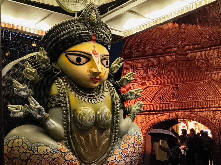 A brightly decorated Durga Puja pandal illuminated at night with crowds gathering