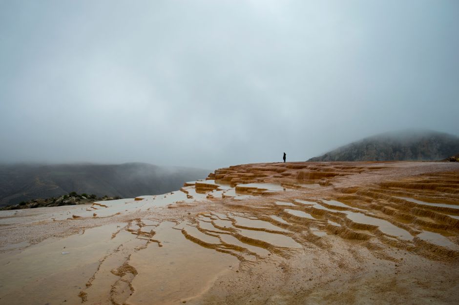 Orange and cream mineral terraces at Badab-e Surt cascading down a dry hillside in Mazandaran