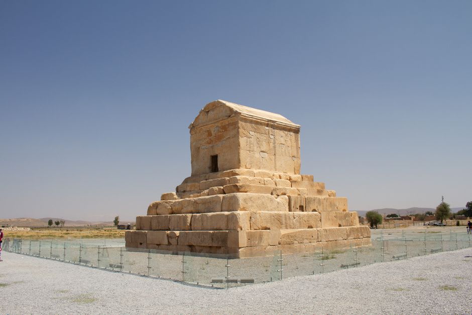 The stepped stone tomb of Cyrus the Great standing isolated in an open field, with mountains visible on the horizon