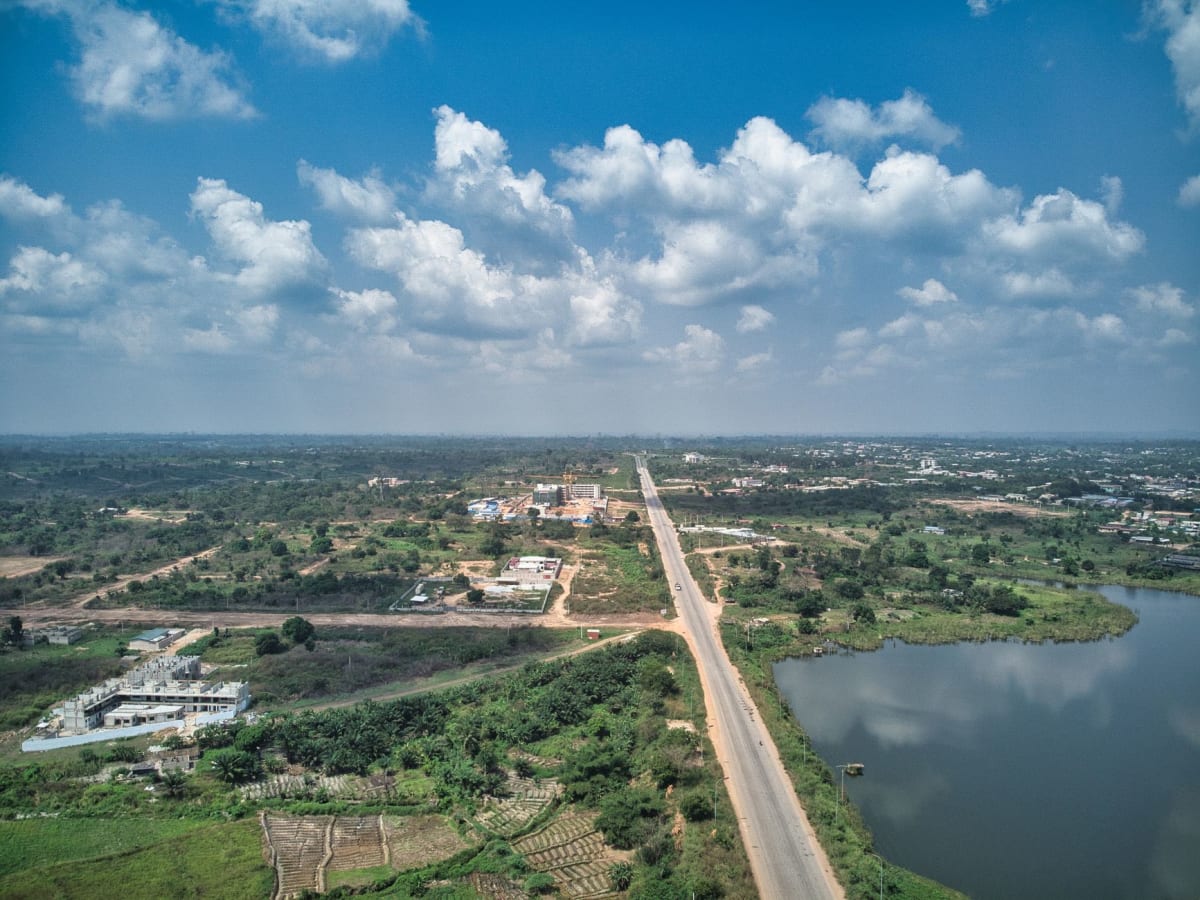 Wide empty government boulevard in Yamoussoukro lined with palm trees and streetlights stretching to the horizon