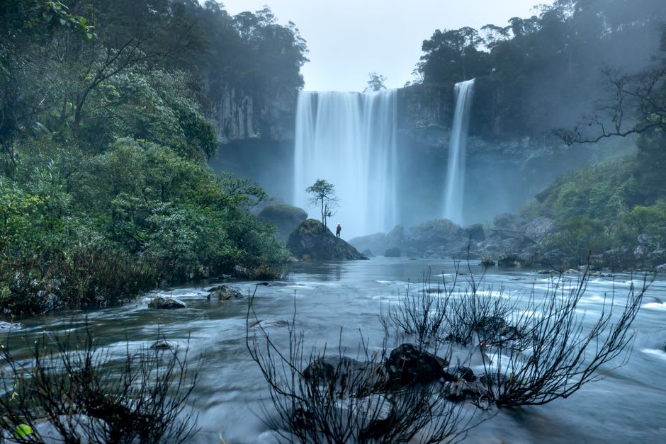 Una cascada envuelta en neblina a lo largo del sendero de Akame 48 Falls, con la luz del sol filtrándose por el dosel del bosque