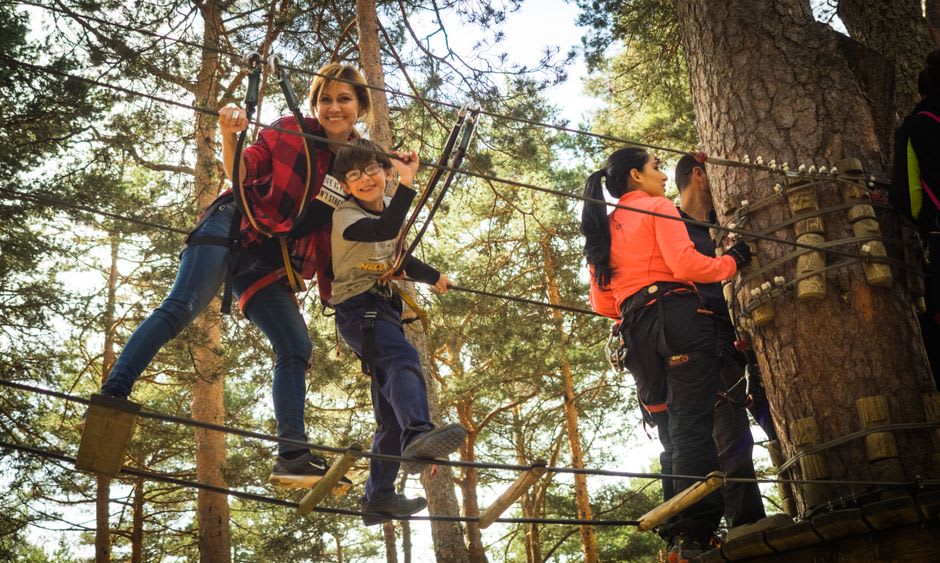 Dos visitantes con trajes de ninja alquilados cruzando un circuito de cuerdas de equilibrio tendido sobre un arroyo en el bosque