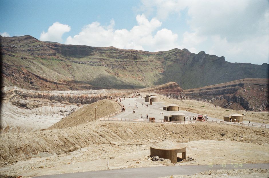 Des chevaux paissant sur la prairie verte et ouverte de Kusasenri dans la caldera d'Aso, un étang de cratère peu profond et des sommets volcaniques derrière eux