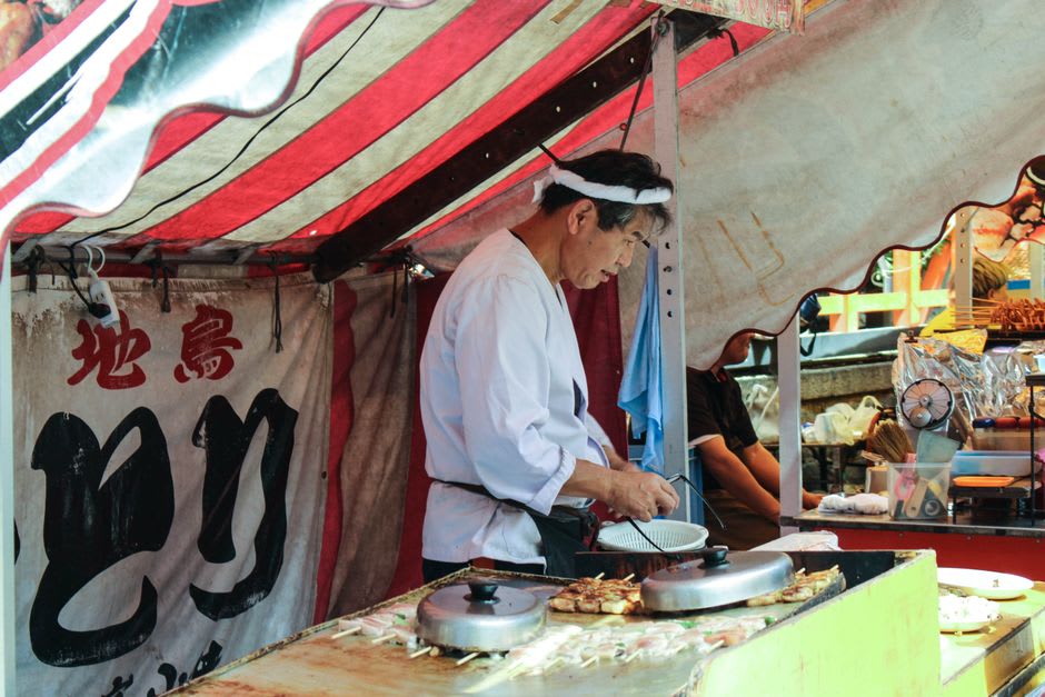 Un cuisinier travaillant derrière le comptoir d'un petit stand yatai à Fukuoka, de la vapeur s'élevant au-dessus d'une rangée de clients assis sous un toit de toile