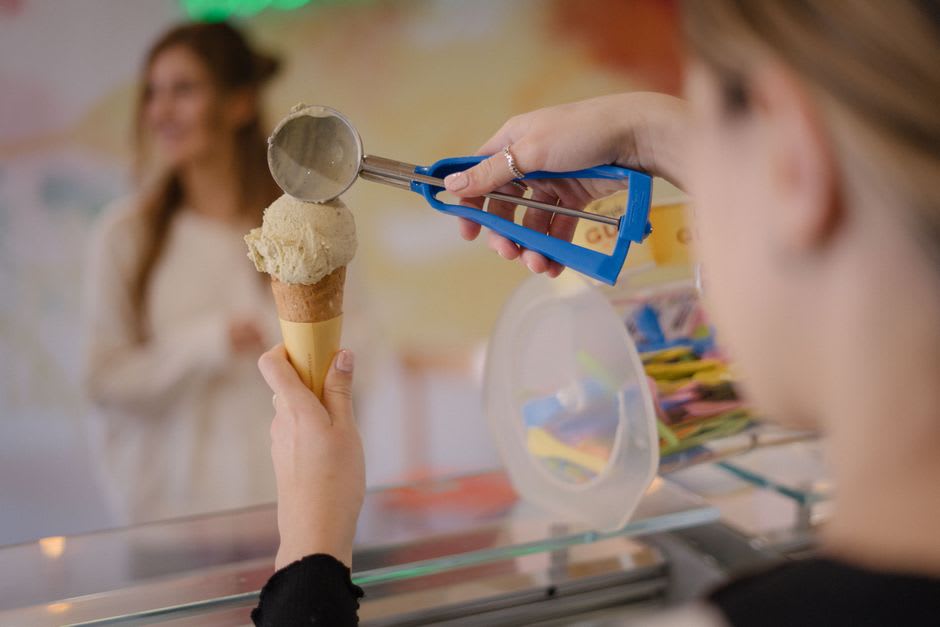 A hand holding a cone of pale golden Jersey-milk soft-serve at a farm shop on Hiruzen Kogen