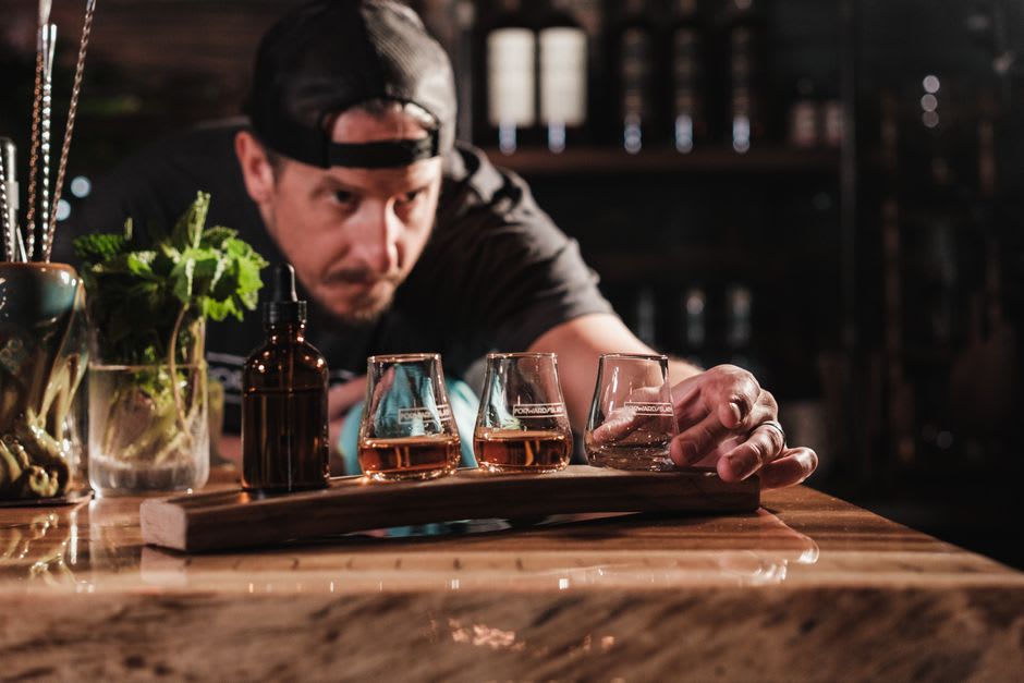 Una selección de botellas de shochu de cebada y pequeños vasos de cata dispuestos en una barra de madera en un izakaya de la isla de Iki