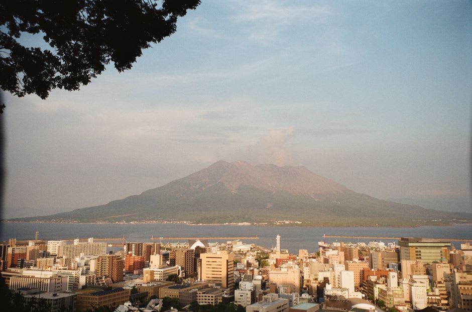 Las laderas oscuras marcadas por la lava del volcán Sakurajima vistas desde el ferry que cruza la bahía de Kagoshima, una columna de ceniza sobre el cono