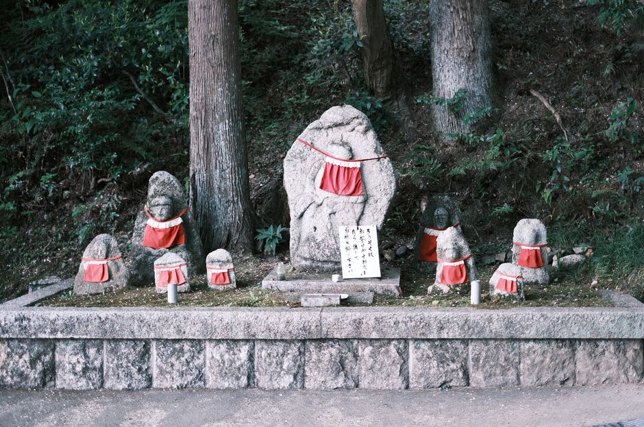 Filas de estatuas de piedra de rakan tocadas por el musgo entre troncos de cedro en el templo Unpenji