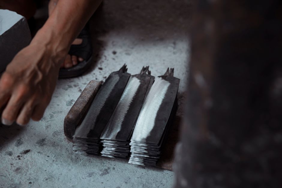 L'intérieur d'une forge à Seki, un maître forgeron et son frappeur travaillant un lingot d'acier incandescent sur l'enclume, dans une quasi-obscurité