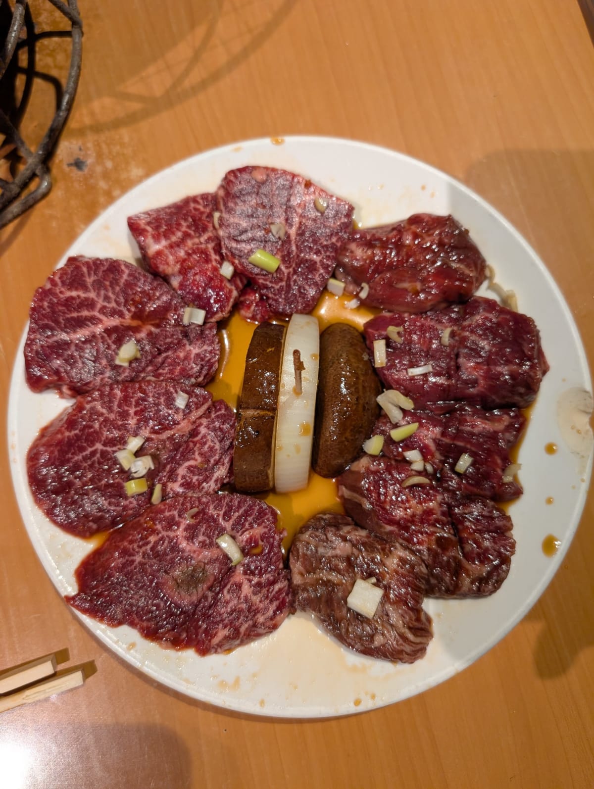 Un plato de yakiniku wagyu — cortes de carne marmoleada dispuestos en círculo alrededor de yema de huevo, listos para la parrilla de carbón