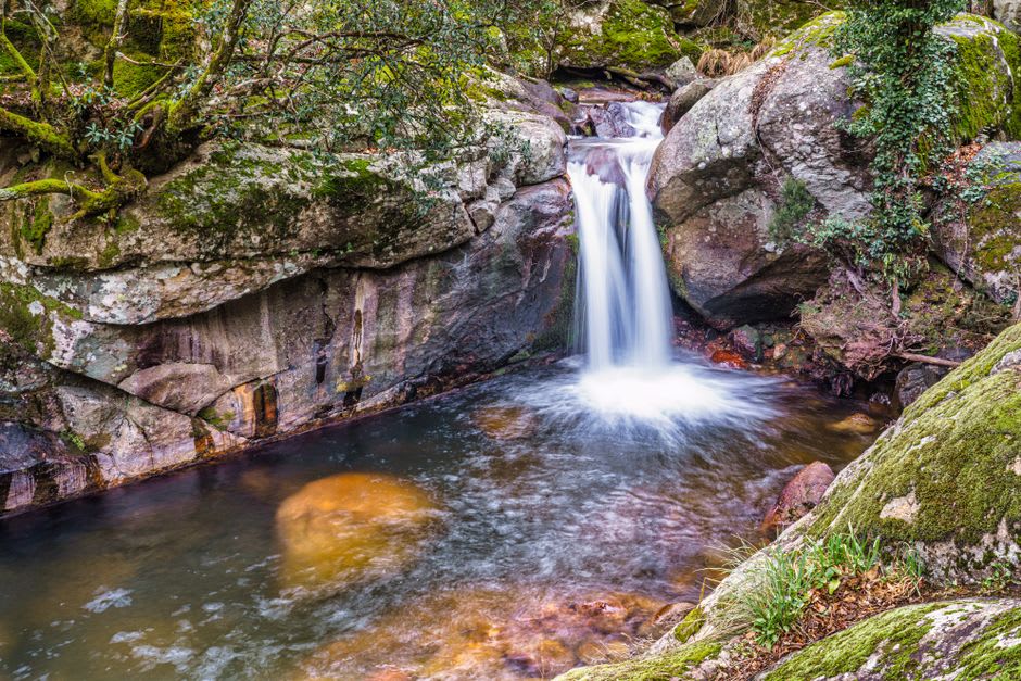 La cascade de Yoro dévalant à travers la roche moussue dans un bassin clair, de la brume s'élevant dans la lumière de l'après-midi