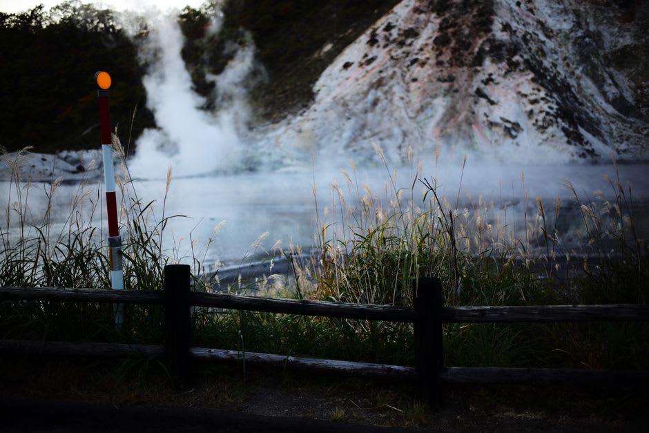 Vapor elevándose desde la salida de una casa de baños tradicional a lo largo del callejón empedrado de Yunotsu, persianas de madera cerradas para la noche