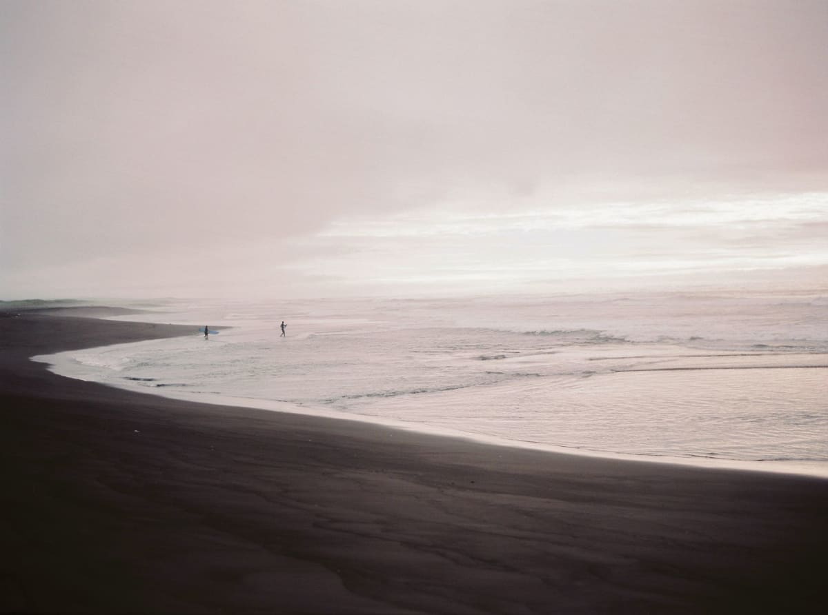 A wide expanse of dark volcanic dunes at Khalaktyrsky Beach with marram grass in the foreground and the grey Pacific surf beyond under a heavy sky