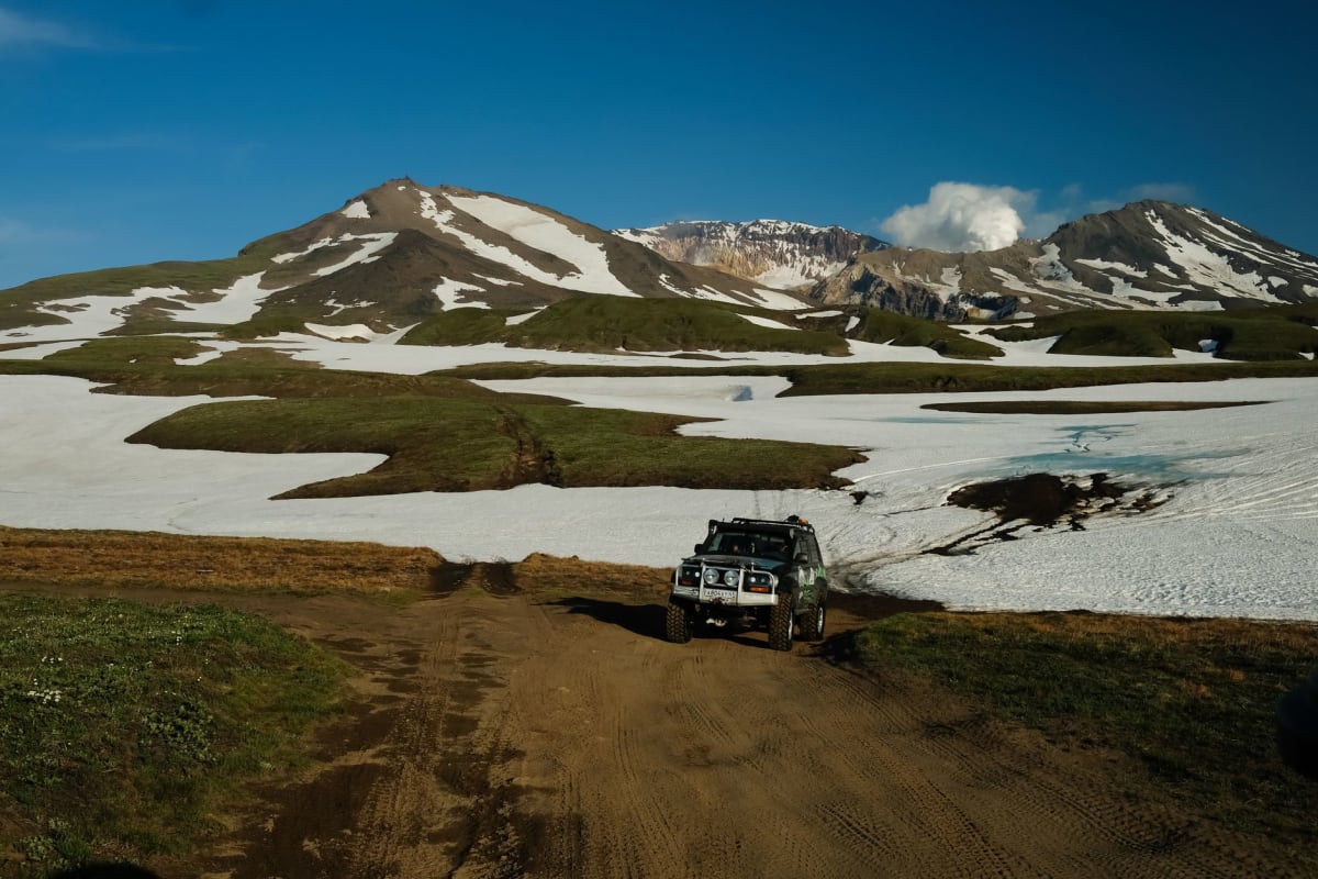 The natural thermal pools at Khodutka, steam rising gently over clear warm water, the tundra valley stretching behind toward distant snow-capped volcanic peaks