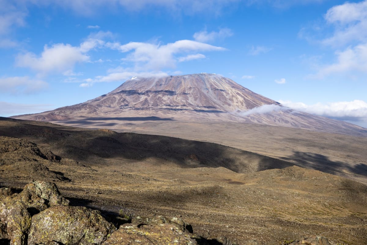 The landscape around Kilimanjaro — volcanic plains stretching toward the mountain's base under a wide African sky