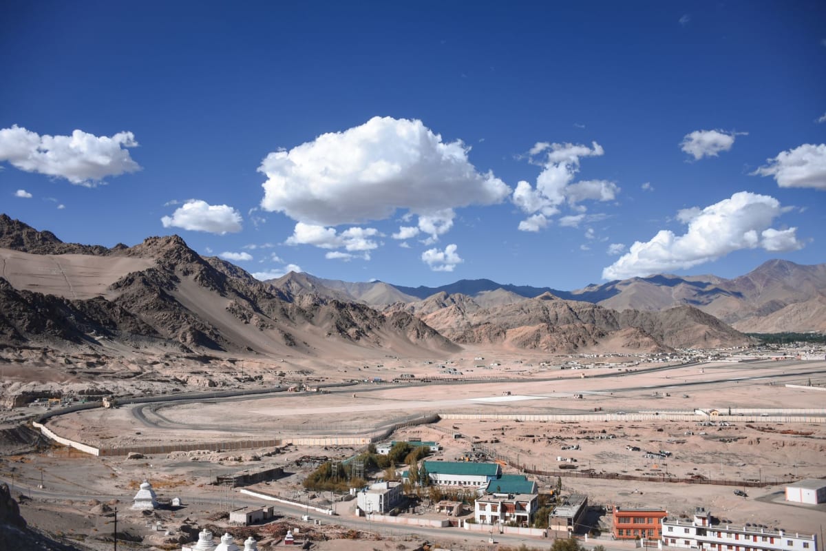 Leh's old bazaar street in morning light, flags strung between buildings, monks and tourists sharing the lane
