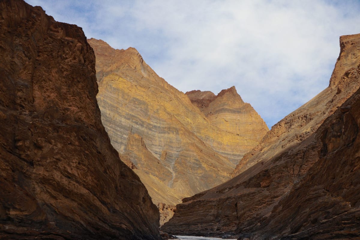 El valle del río Zanskar en verano con campos verdes de cebada en las orillas aterrazadas y ruinas de monasterios en lo alto del acantilado, picos desnudos elevándose detrás