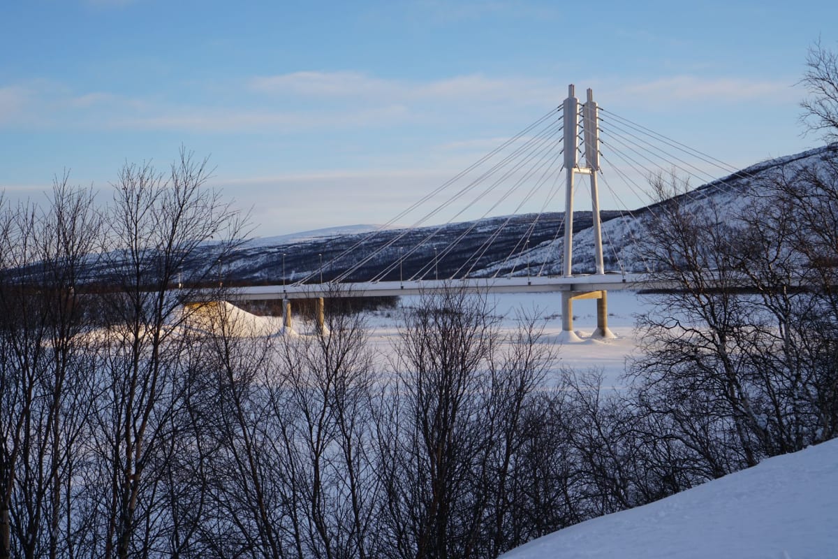 Une petite église sami en bois à Utsjoki, des bouleaux enneigés l'entourant, ciel hivernal pâle au-dessus de la crête de fell