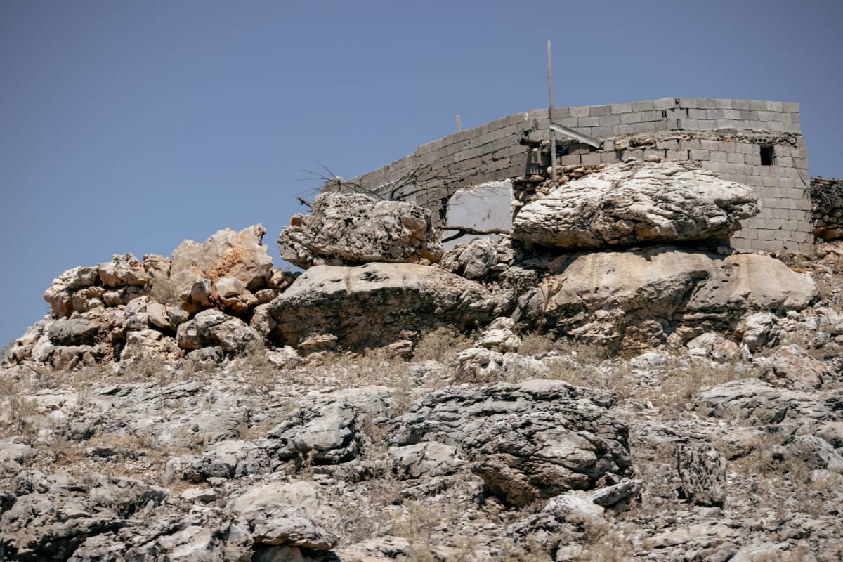 El Cementerio de Guerra alemán en Tobruk, cruces de basalto negro emparejadas sobre tierra oscura, el muro de recinto bajo visible al fondo