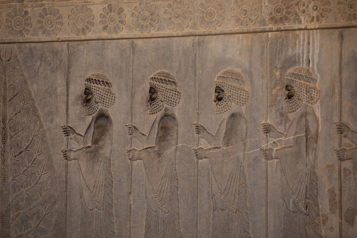 Low stone ruins of the Assyrian palace at Nimrud, carved stone reliefs partially visible in the excavated throne room walls, a solitary archaeologist recording findings in the morning light