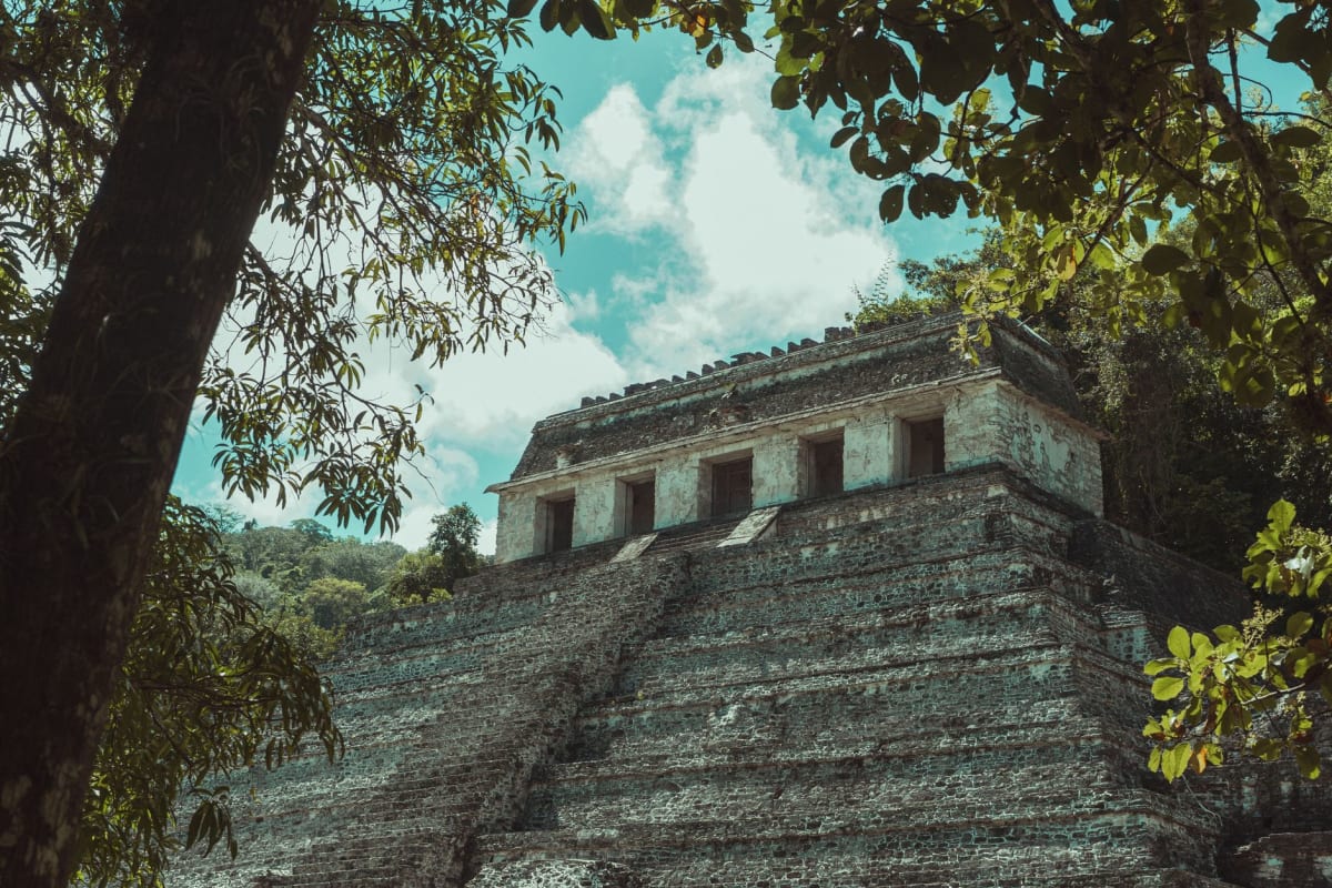 A Lacandon Maya family outside their palm-thatched house near the Bonampak site, the traditional white tunic dress of the Lacandon visible, the jungle clearing behind the house, the Lacandona rainforest surrounding the community
