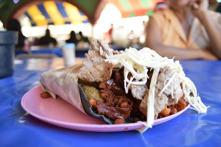 A plate of machaca con huevo at a Linares market comedor, flour tortillas on the side, a cup of coffee, the covered market visible behind