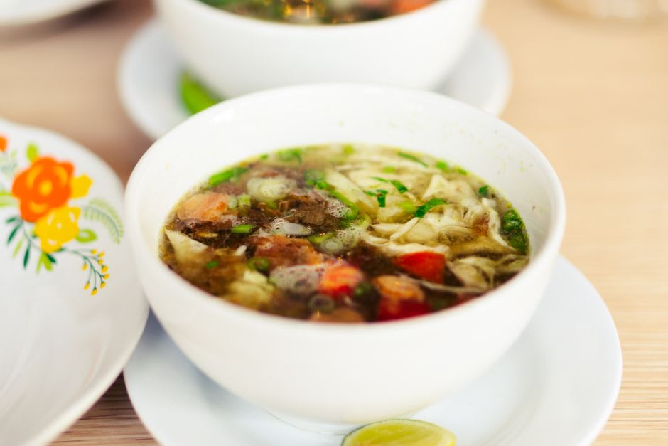 Un tazón de caldo de pollo chino en un restaurante de La Chinesca en Mexicali, caldo transparente con verduras y la profundidad particular de un fondo estilo chino de cocción larga