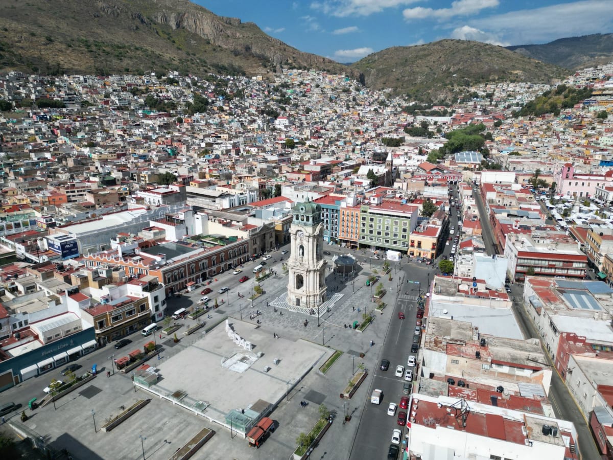 An Pachuca paste vendor's cart near the Reloj Monumental, the pastries lined up under a cloth, their crimped tops visible, a hand reaching for one, the clock tower visible behind in the late morning light