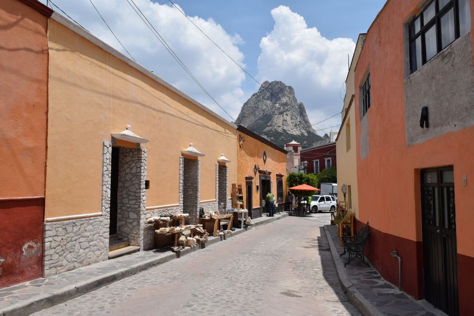 Le marché artisanal du village de Bernal un matin de week-end, les étals de textiles et de confiseries sous les portiques coloniaux, la Peña de Bernal visible au-dessus des toits au bout de la rue du village