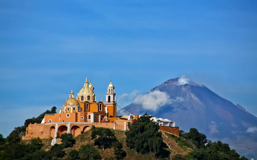 Las torres gemelas de piedra de la catedral de Puebla y la cúpula recubierta de Talavera de la Capilla del Rosario visibles sobre los edificios coloniales que rodean la plaza principal