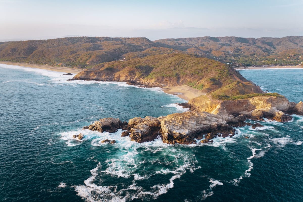 Une panga se dirigeant vers les Islas Marietas depuis Punta Mita, les formations rocheuses de l'île devant, un souffle de baleine à bosse visible sur la gauche, la baie de Banderas d'un bleu profond dans la lumière de janvier