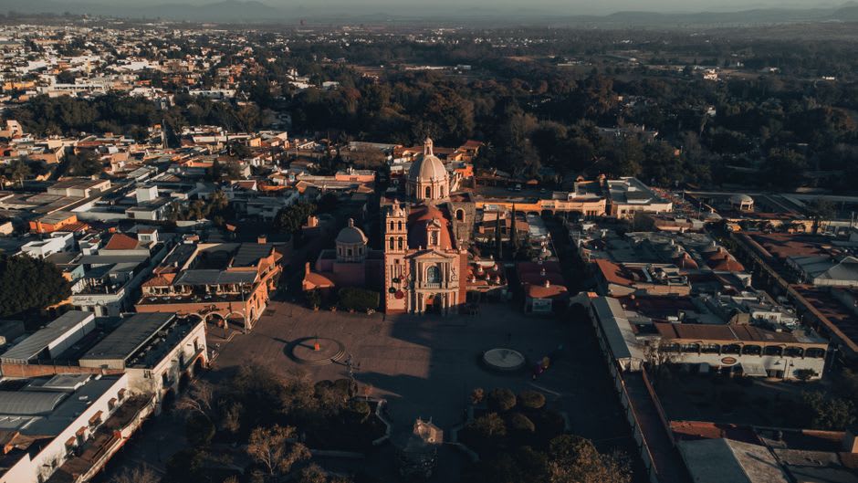 Église coloniale et place de San Joaquín au crépuscule, les collines de la Sierra Gorda s'élevant derrière les toits