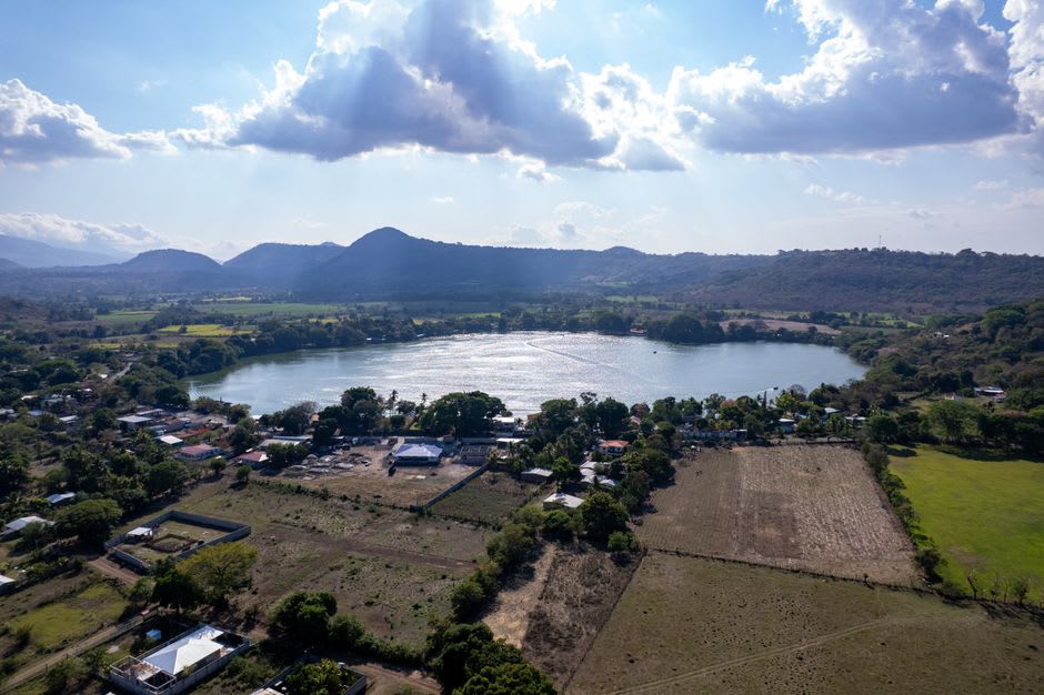 The San José reservoir north of Soyaniquilpan, a wide calm sheet of water reflecting a pale sky, cattle at the bank and low dry hills beyond