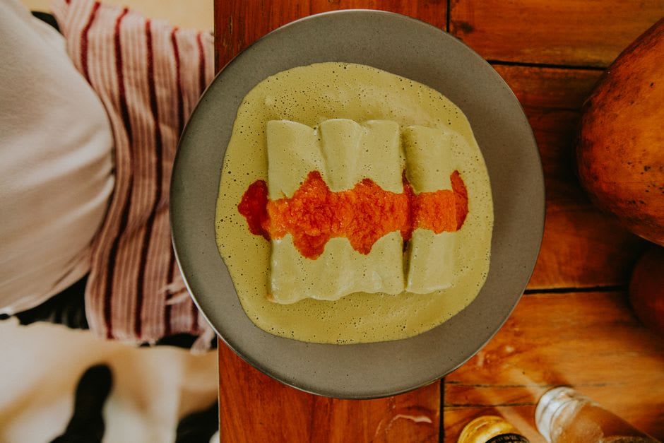 Une assiette d'enchiladas huastecas dans un comedor de Tamasopo — tortillas de maïs à la salsa roja avec pomme de terre, fromage frais et avocat — sur une table en plastique avec un verre d'agua fresca
