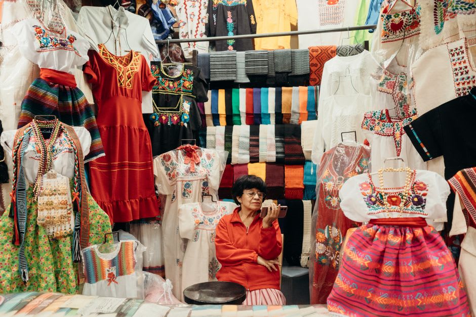 Paneles de tela tenango bordados a mano exhibidos en el mercado del pueblo, mostrando venados y aves sobre un fondo carmesí