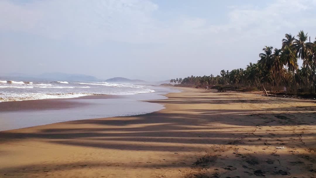 Playa La Ropa in Zihuatanejo, the long crescent of beach with the calm bay water below the vegetated headland, fishing boats at anchor in the middle distance, the Pacific entrance to the bay beyond