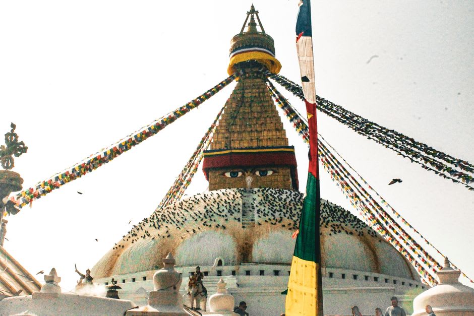 Peregrinos y monjes caminando la kora alrededor de la base de la estupa de Boudhanath al amanecer, ruedas de oración bordeando el muro a su lado