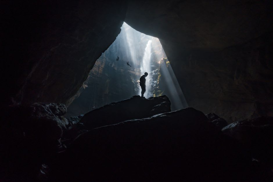 Underground river visible through a gap in the cave rock inside Gupteshwor Cave, illuminated by a single hanging bulb