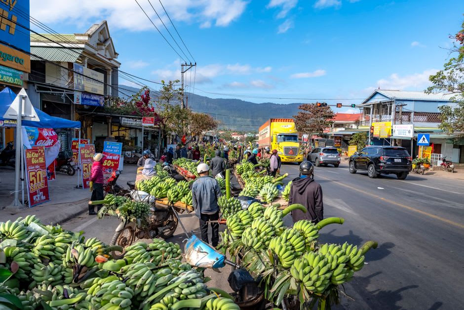 Busy market street in Melamchi Pul Bazaar with loaded buses and vendors selling produce from roadside stalls