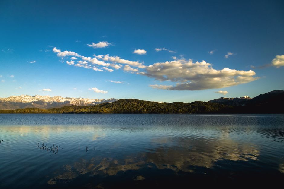 Sentier de terre serpentant le long du rivage du lac Rupa à travers des rizières en terrasses, avec des collines lointaines sous un ciel couvert
