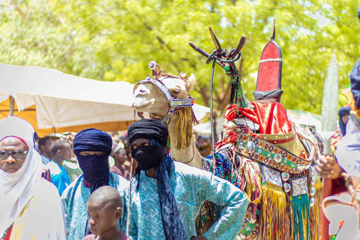 Le marché aux arachides de Maradi — des sacs en jute empilés contre un mur bas, des hommes qui commercent dans la lumière de midi qui a rendu la poussière dorée