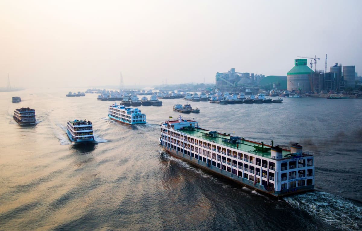 The colonial waterfront of Port Said, wooden verandas painted in faded green and blue overhanging the seafront streets, a container ship visible in the canal channel behind